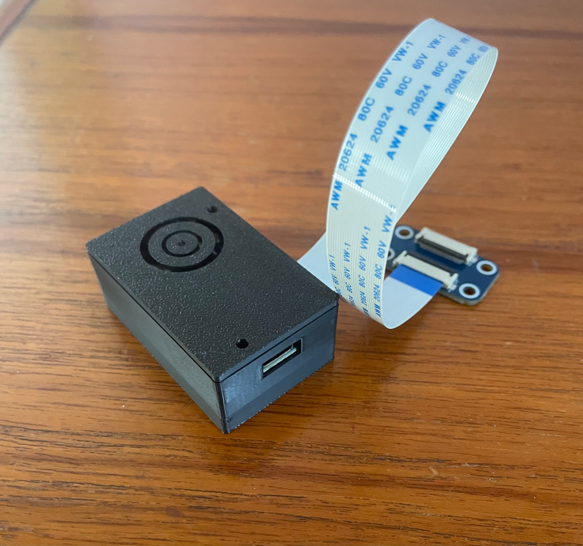 The ESTER programmer in its black 3D-printed enclosure with a USB-C cable and the e-paper ribbon cable attached